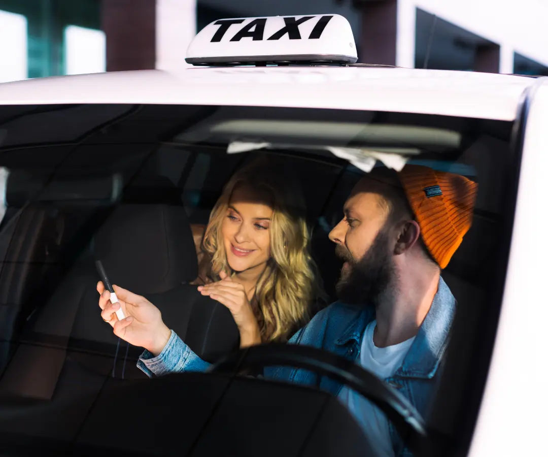 En man sitter i förarsätet i en taxi och visar något för en kvinna i baksätet på en översättare som han håller i handen. Kvinnan ler intresserat. En taxiskylt syns på bilens tak.